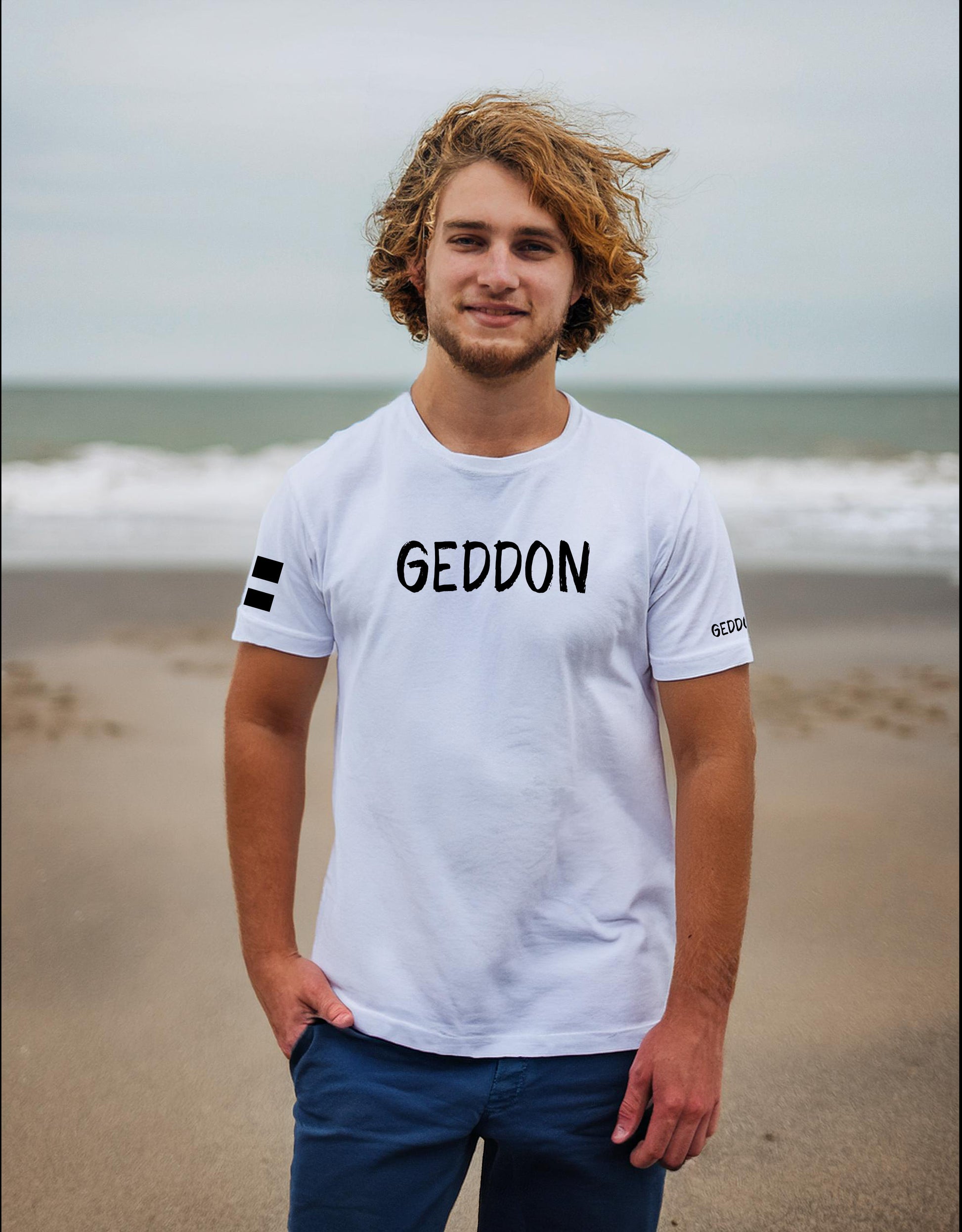 Model wearing a white t-shirt with "GEDDON" in bold black text on the chest, featuring a Cornish flag on the sleeve.