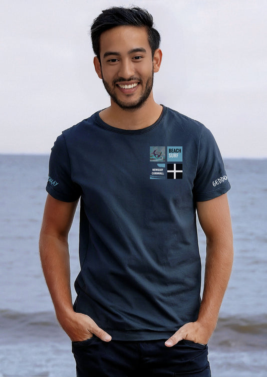 Newquay Surf T-shirt on model, navy, featuring surfer design, 'BEACH SURF' text, 'NEWQUAY CORNWALL' with surf splash, and Cornish flag.